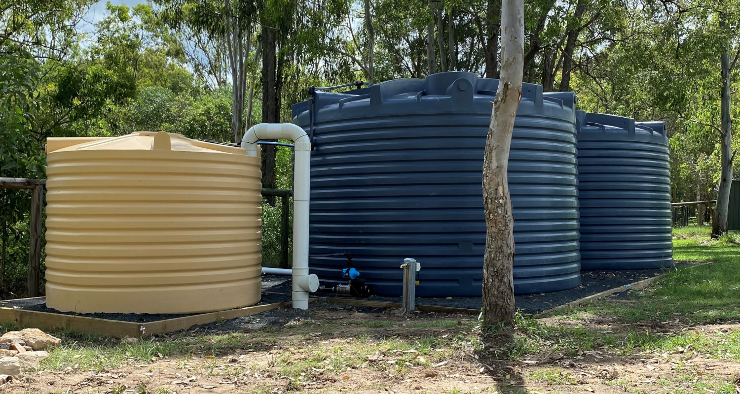 Three water tanks standing next to each other with white pipe on closest.