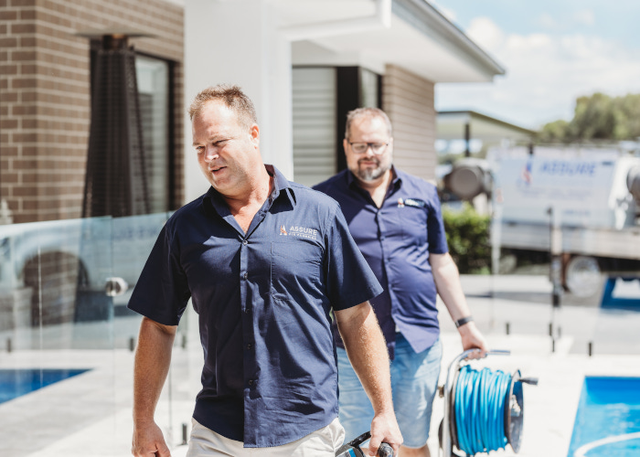 assure plumbers walking beside a pool