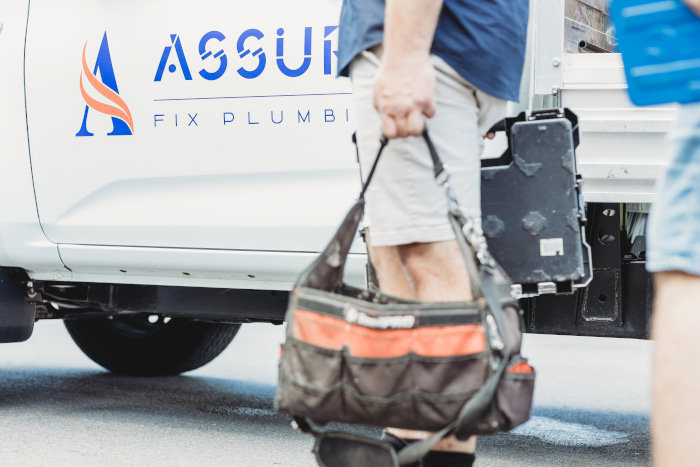 Assure fix plumbers walking past their car and holding bag filled with tools