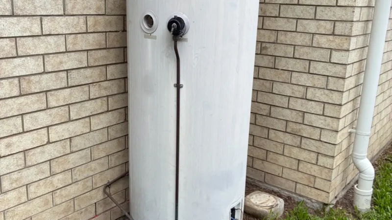 Hot water system replacement with exposed tank, wiring, and plumbing tools on grass