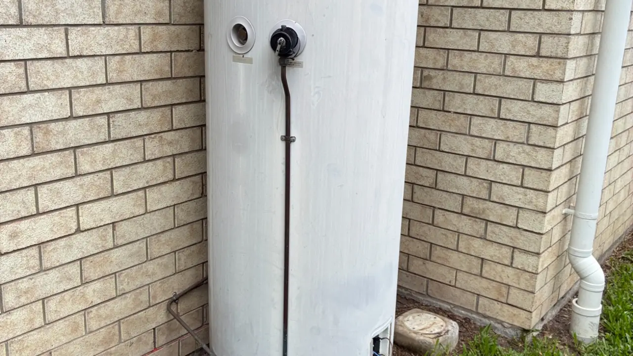 Hot water system replacement with exposed tank, wiring, and plumbing tools on grass