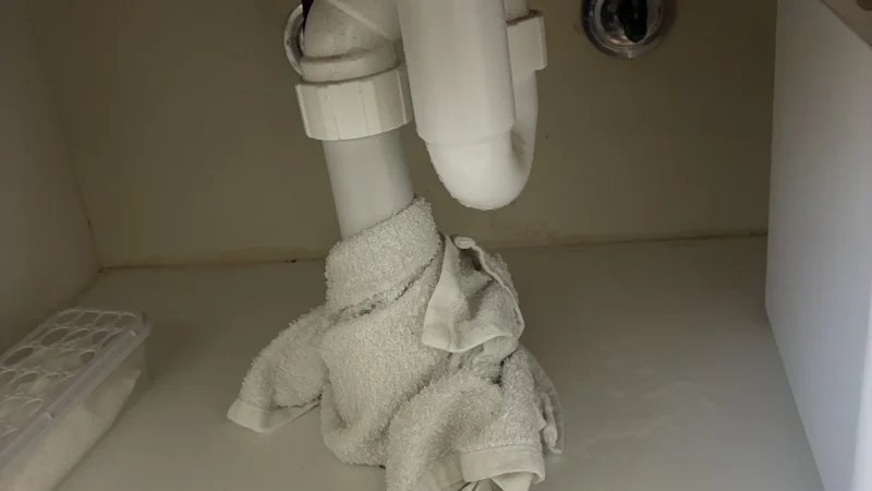 DIY plumbing mistake under sink with leaking pipes and temporary towel fix