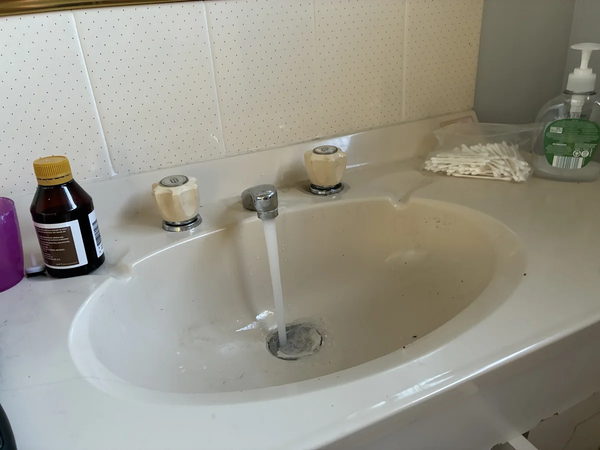 Leaking bathroom tap with water running into the basin from older-style twin handle taps
